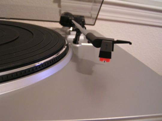 Close-up photo of the cartridge and stylus on the Ion Audio TTUSB05 turntable. Platter with mat is partially visible on left side of photo.