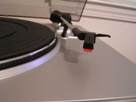 Close-up photo of the cartridge and stylus on the Ion Audio TTUSB05 turntable. Platter with mat is partially visible on left side of photo.